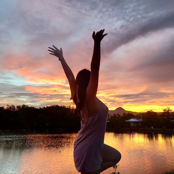 Person doing a standing yoga pose against a sun petal colored background.
